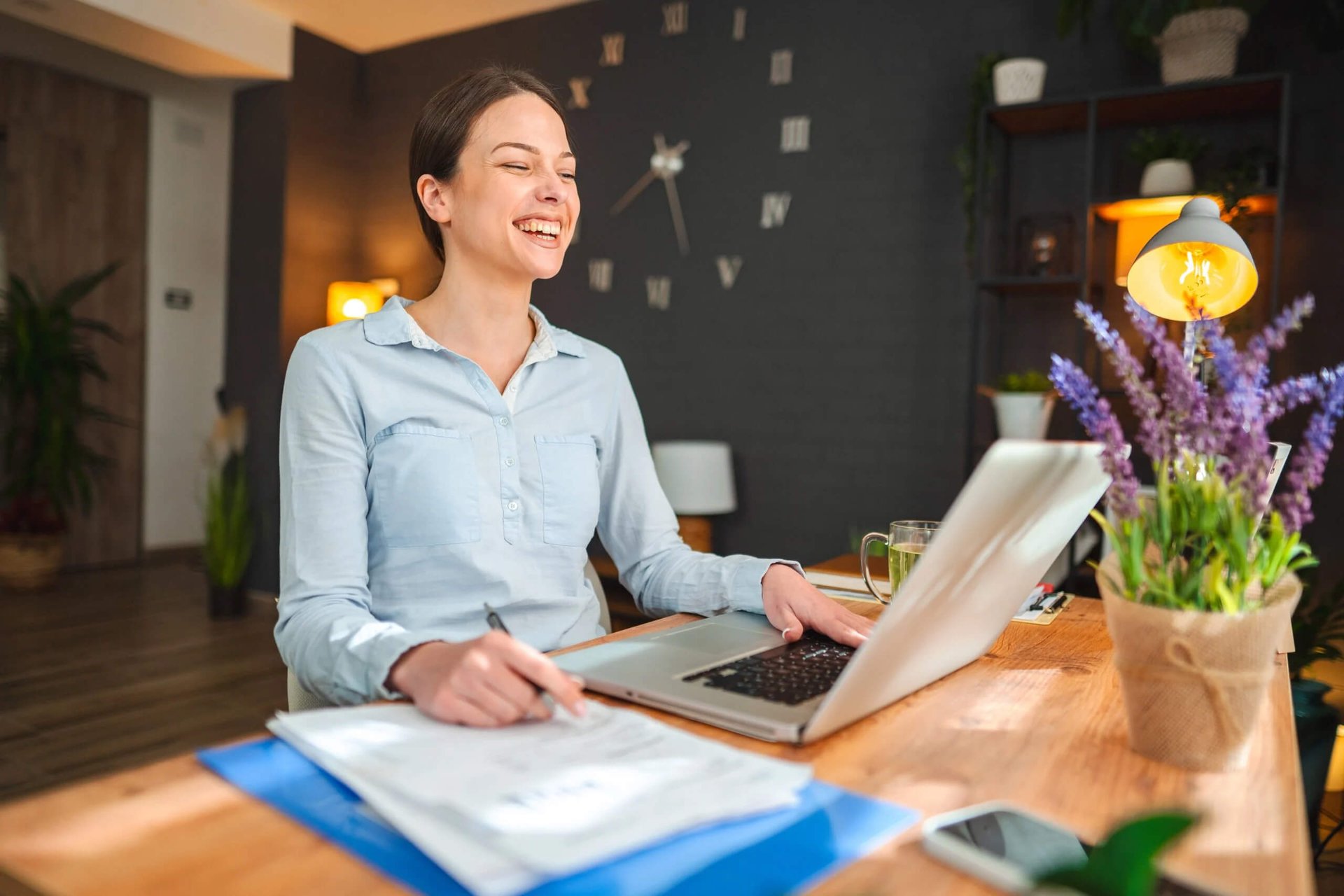Glad ung kvinna antecknar på papper framför laptop