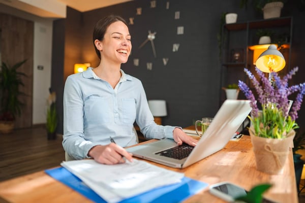 Glad ung kvinna antecknar på papper framför laptop