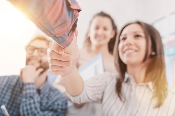 Leende kvinna skakar hand med person som inte syns i bild.