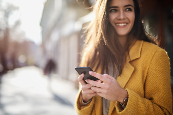 Smiling young woman in urban environment holding a cell phone.
