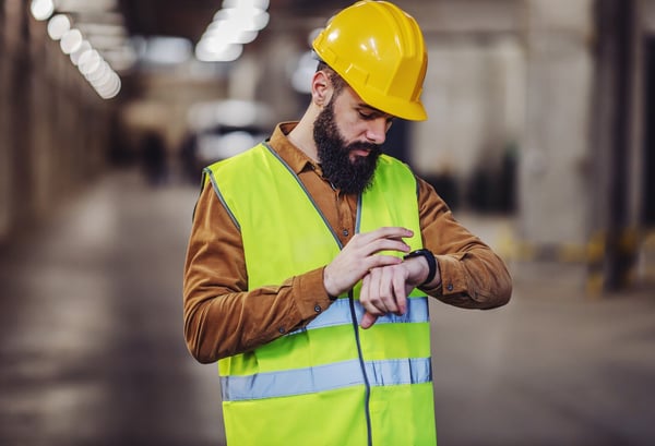 Man med reflexväst och arbetshjälm tittar på sin klocka.