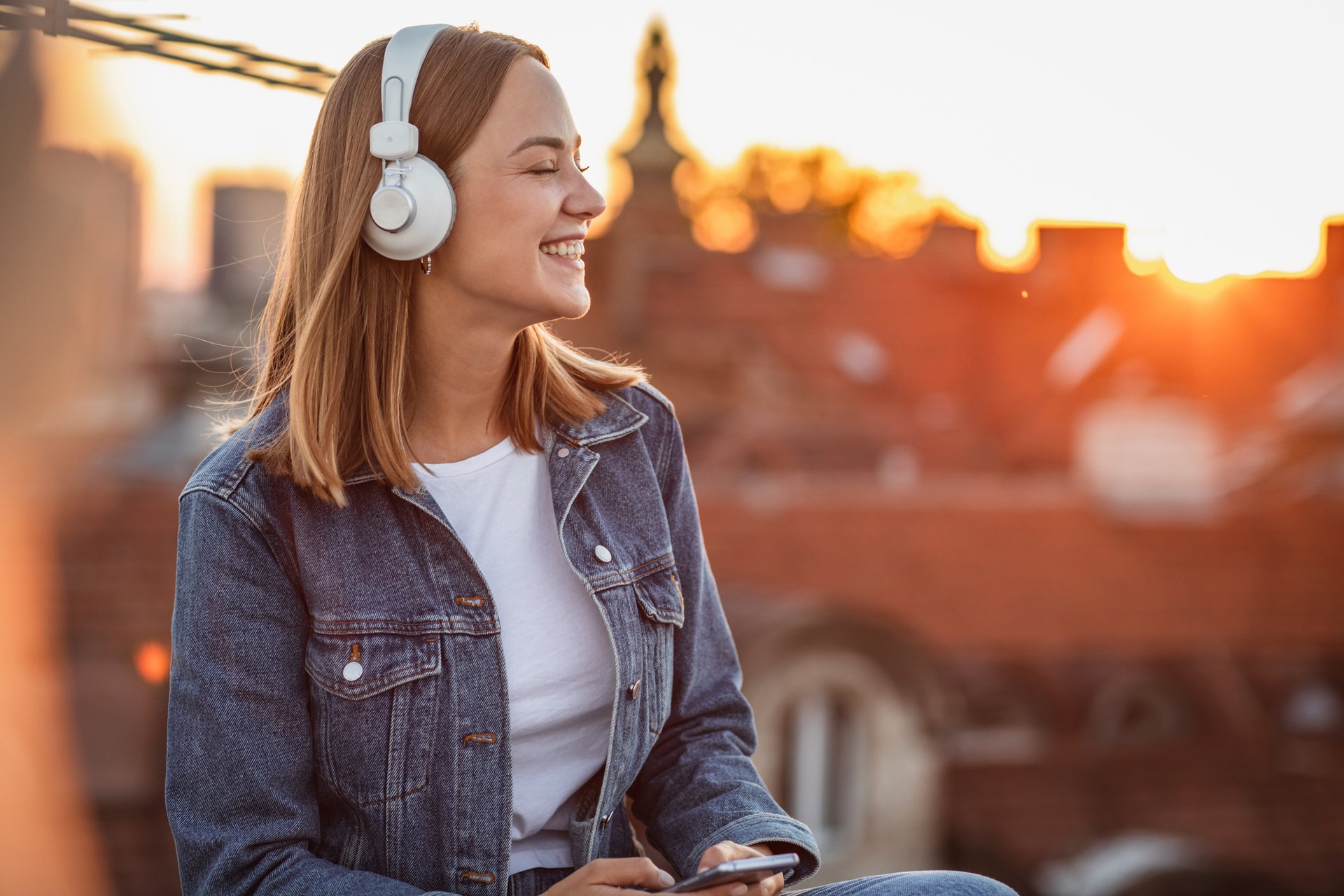 Smiling woman with headphones in front of a city skyline.