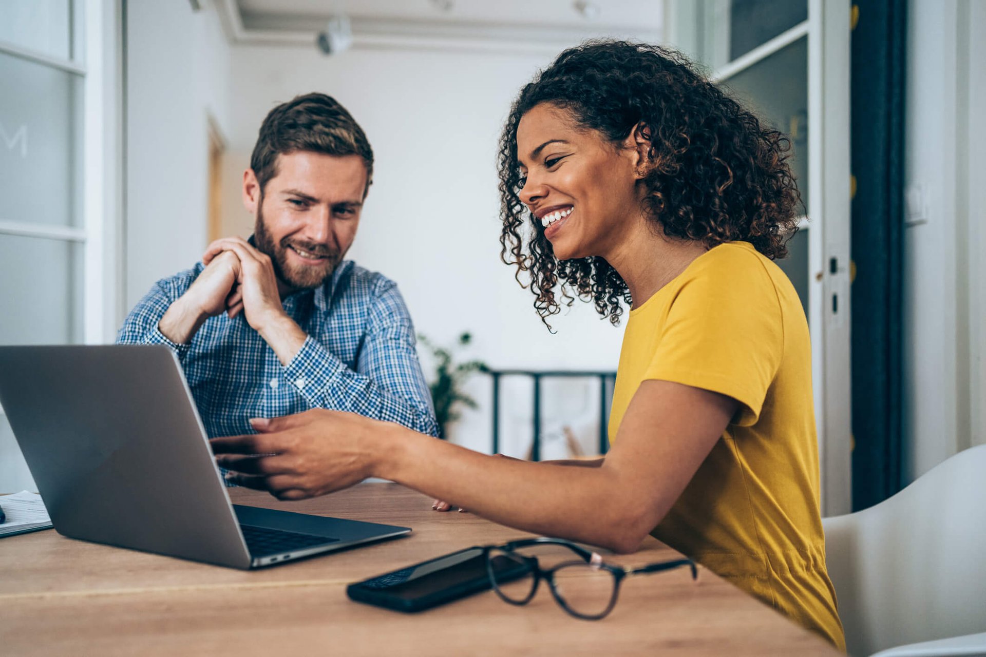 two people sitting and looking at a computer screen, smiling