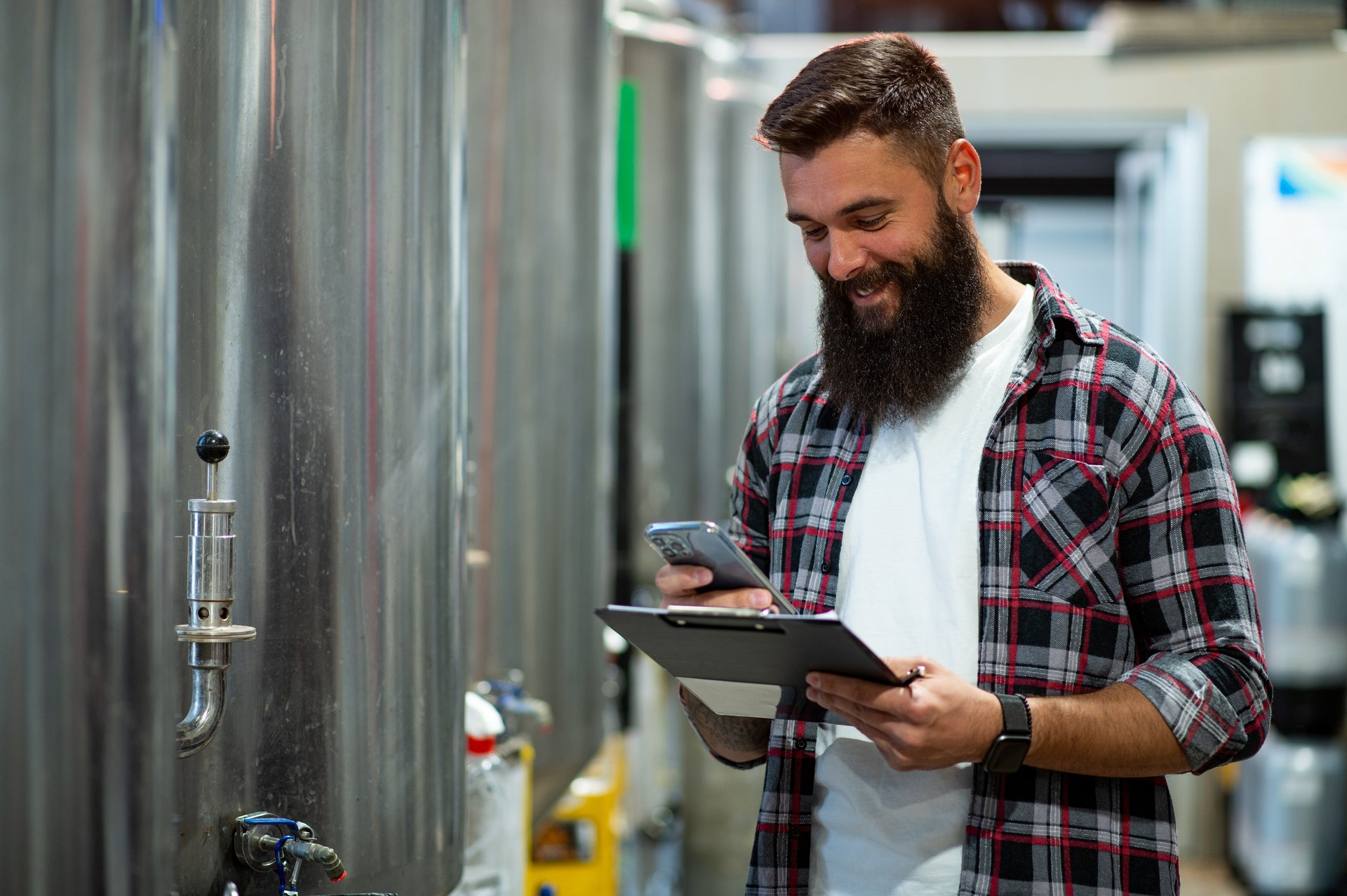 Smiling man on an industry premises looking at his cellphone.