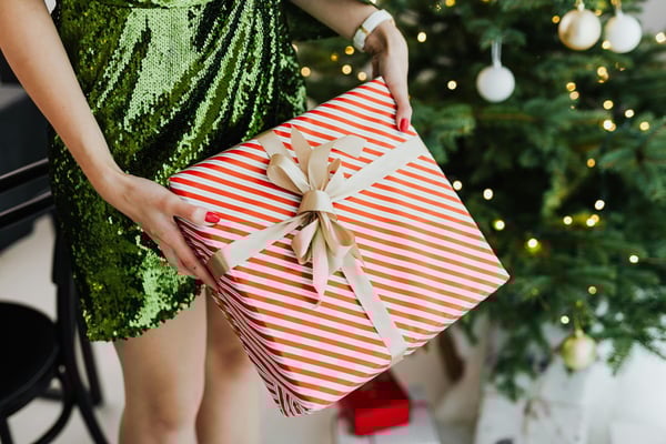 A woman in a festive dress holds out a beautifully wrapped Christmas present.